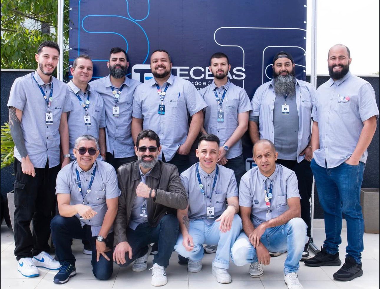 Equipe Tecbas reunida em frente ao painel da empresa